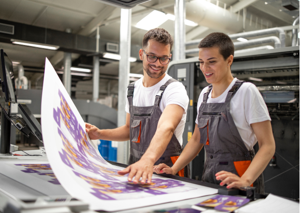 Two workers at a printing facility review a printed poster